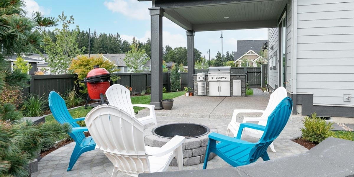 stone fire pit with adirondack chairs and outdoor kitchen on backyard patio
