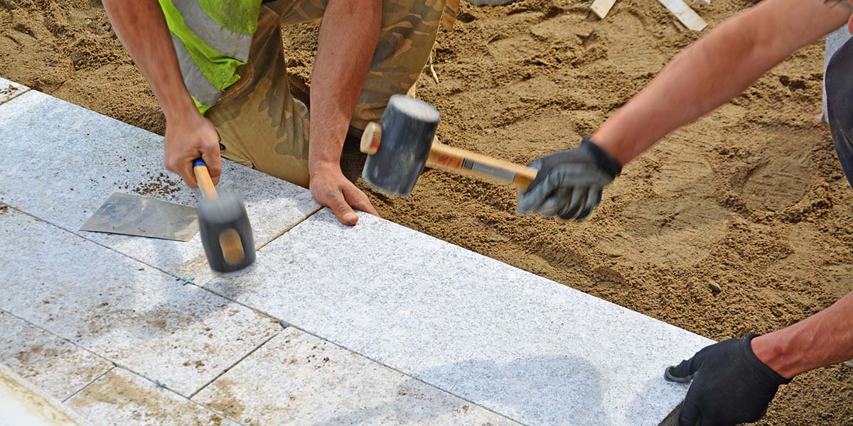 two contractors putting together a paver patio in a backyard