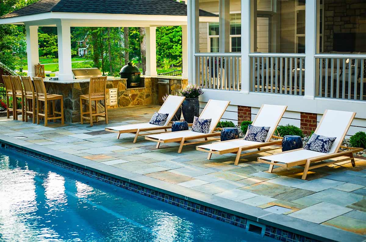 u shaped outdoor kitchen under a gazebo next to pool chairs next to a pool