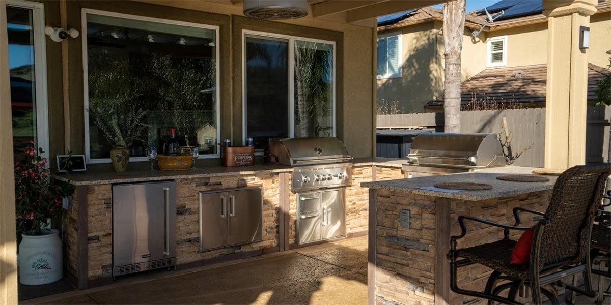 u shaped outdoor kitchen with multiple grills and a refrigerator