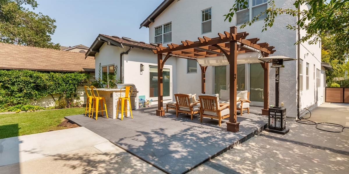 white house with pergola seating area and outdoor kitchen in backyard