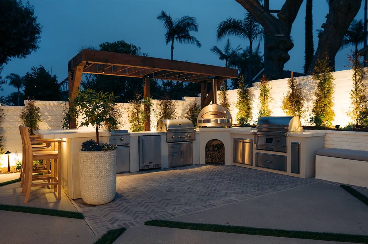 white u-shaped outdoor kitchen illuminated by backlighting in the evening