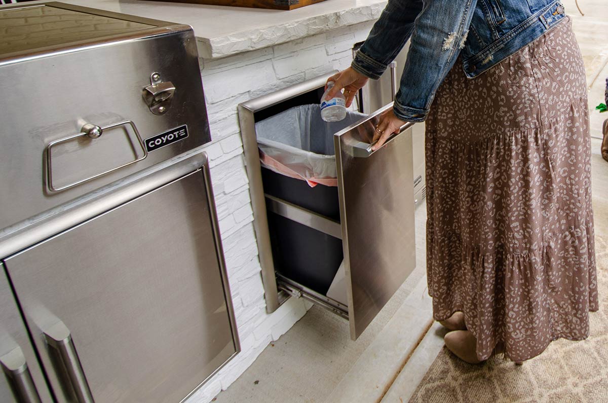 woman opening pull out trash in outdoor kitchen