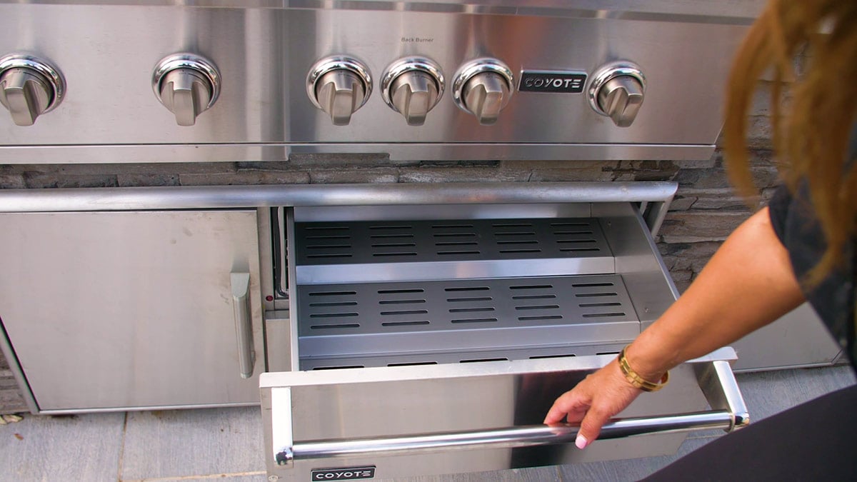 woman opening warming drawer in outdoor kitchen