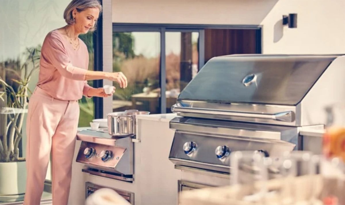 woman using side burner on l shaped twin eagles outdoor kitchen