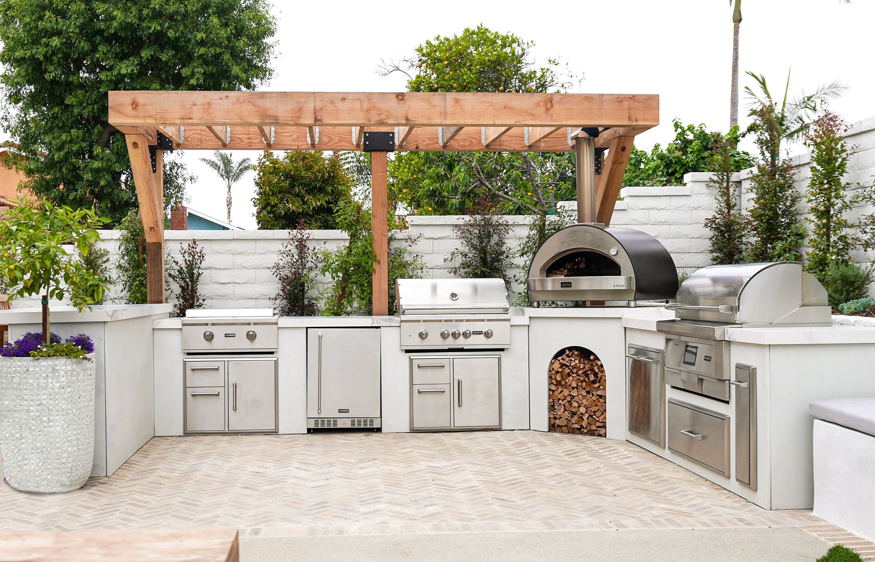 mike pyles u shaped outdoor kitchen with pizza oven, refrigerator, plenty of drawers, and two grills in the backyard of his house